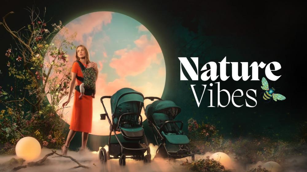 Kobieta stoi przy wózku, ma w nosidle dziecko, stoi na tle koła na którym jest różowo-błękitne niebo. Kolekcja nature vibes kinderkraft