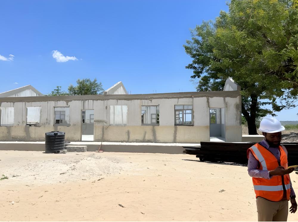 Budowniczy w kasku stojący na tle gołych ściany szkieletu nowego budynku szkoły w Mozambiku