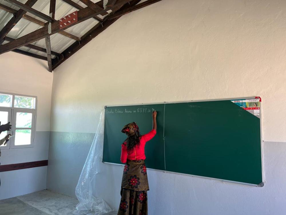Nauczycielka pisząca kredą na nowej tablicy w odbudowanej szkole w Mozambiku
