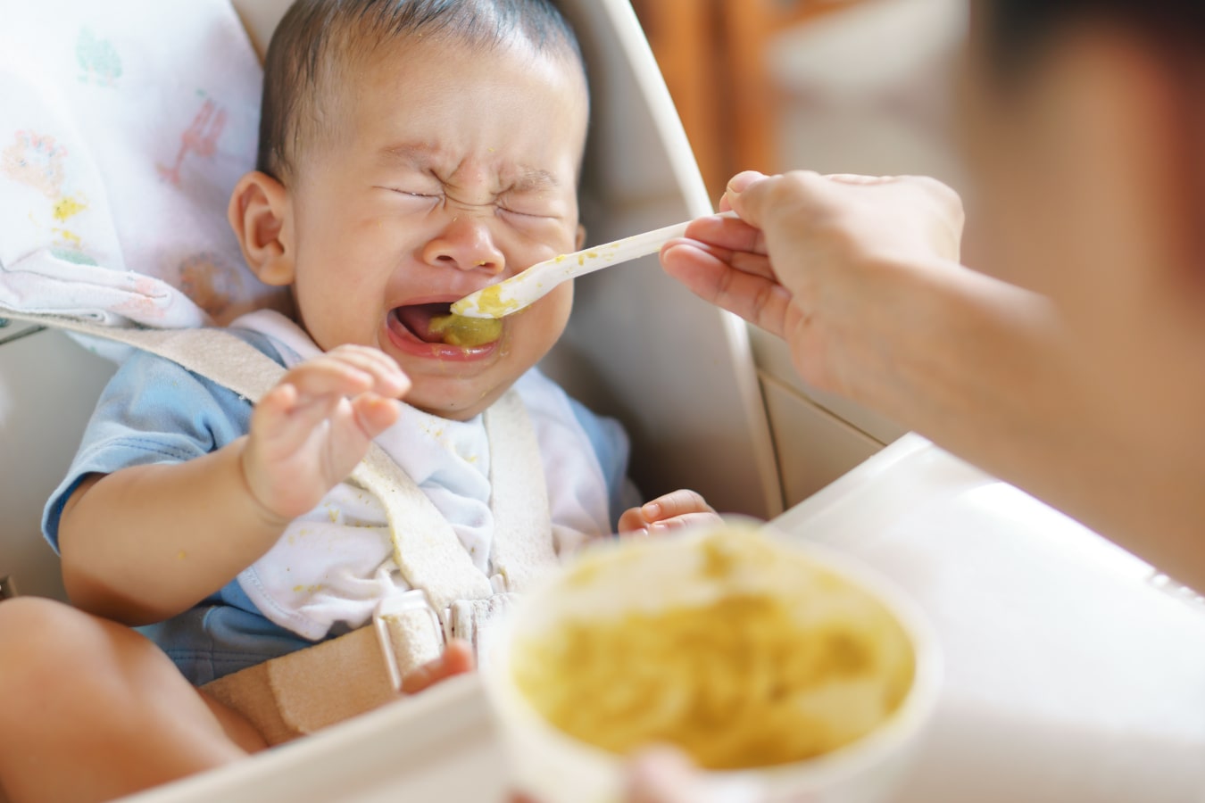 Dziecko siedzi zapięte w krzesełku do karmienia, nie chce jeść z łyżeczki i płacze
