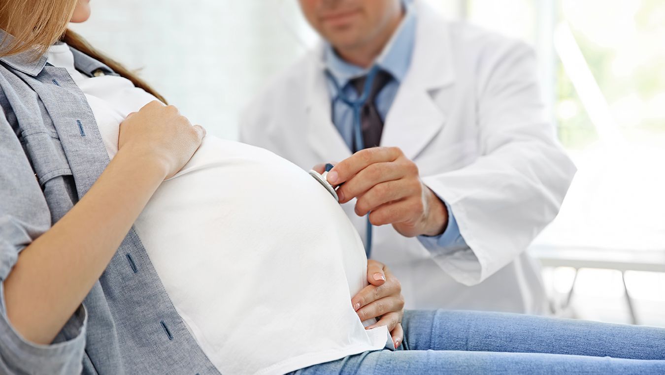 Lekarz w białym fartuchu przykłada stetoskop do ciążowego brzucha kobiet