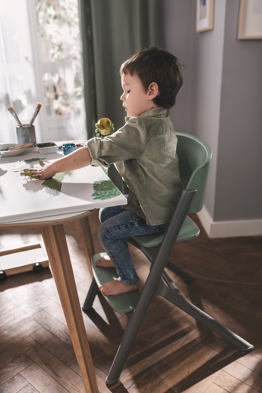 Chłopczyk siedzi na krzesełku do karmienia LIVY Kinderkraft, maluje palcami na płótnie, jest skupiony i zrelaksowany