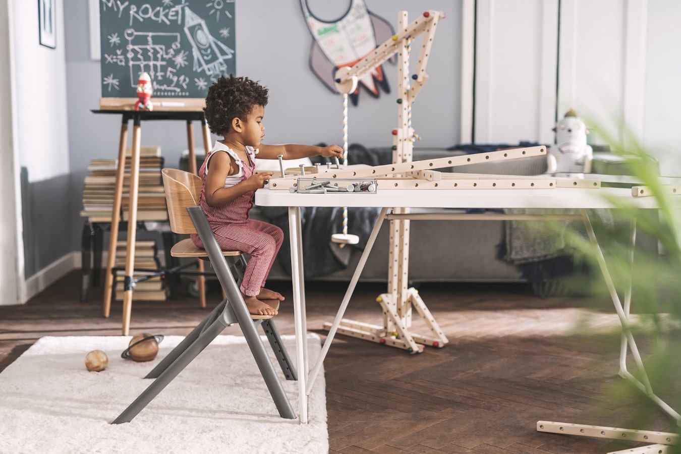 Mały chłopczyk o czarnych włosach buduje konstrukcję z drewna, jest bardzo skupiony, siedzi na krzesełku LIVY Kinderkraft
