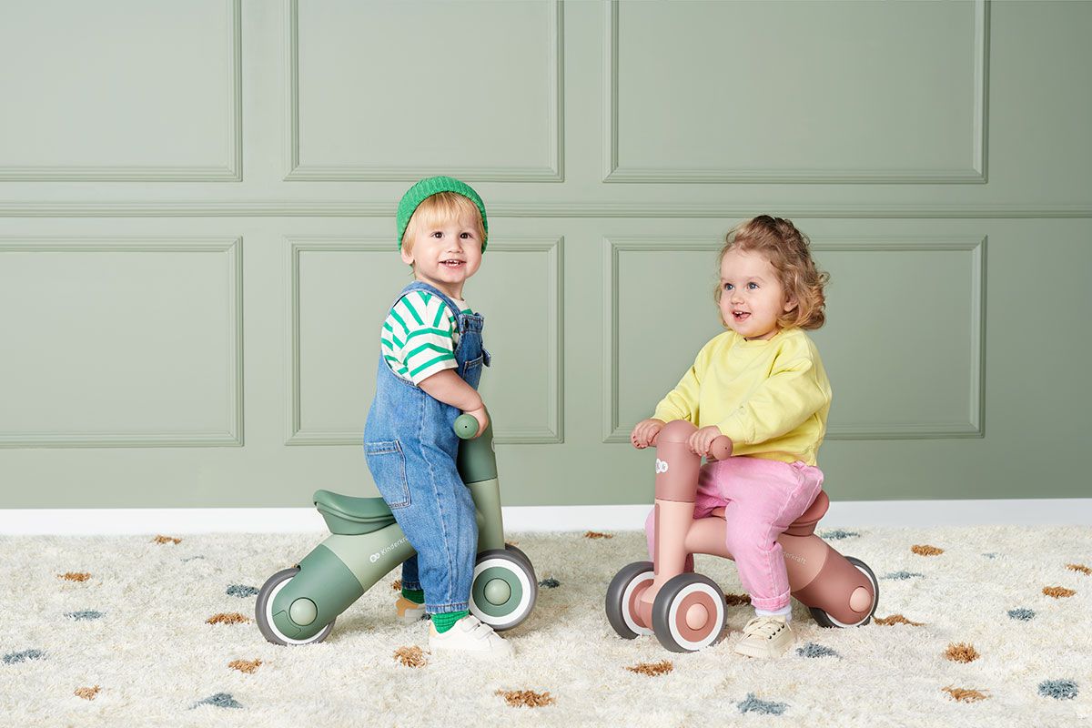Dwoje dzieci siedzi na rowerkach MINIBI na tle ściany. 