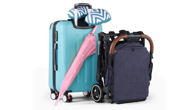 Złożony wózek NUBI stoi obok walizki, o którą oparty jest parasol. Przez rączkę przewieszona jest poduszka podróżna. 