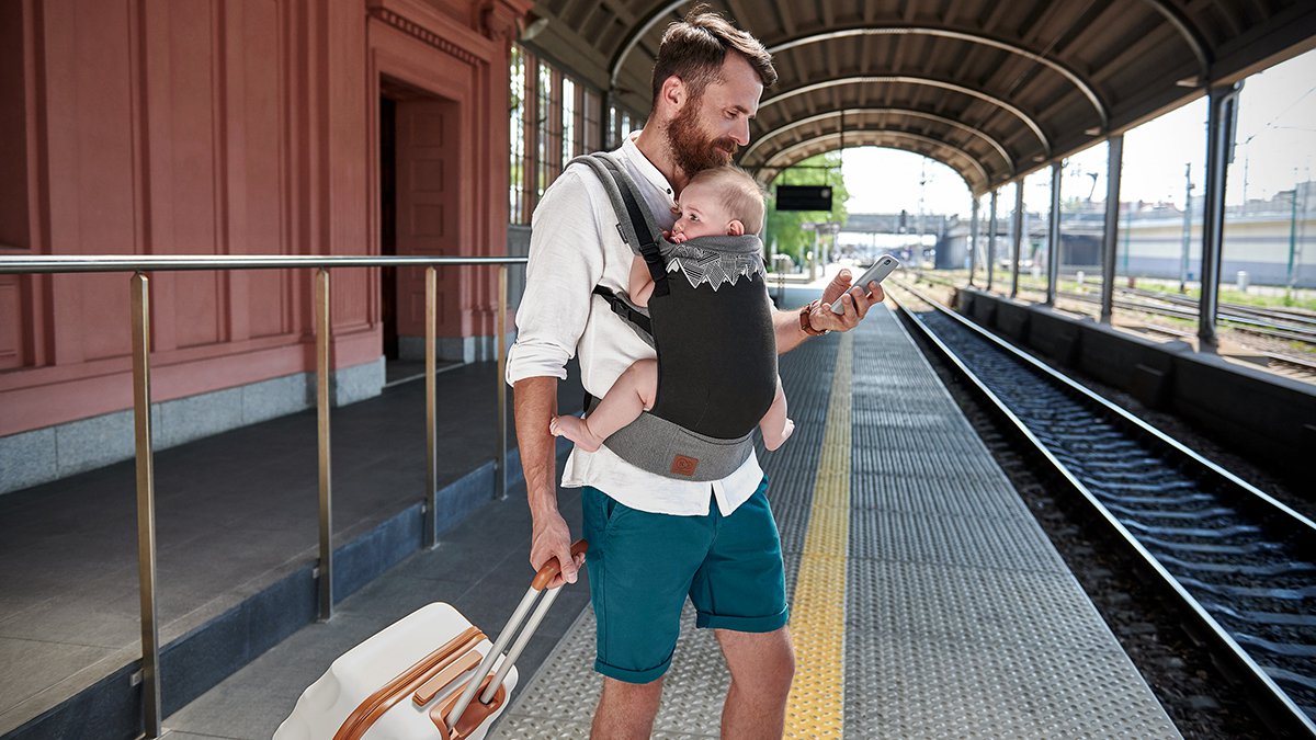 Ojciec stoi na peronie z dzieckiem w ergonomicznym nosidełku