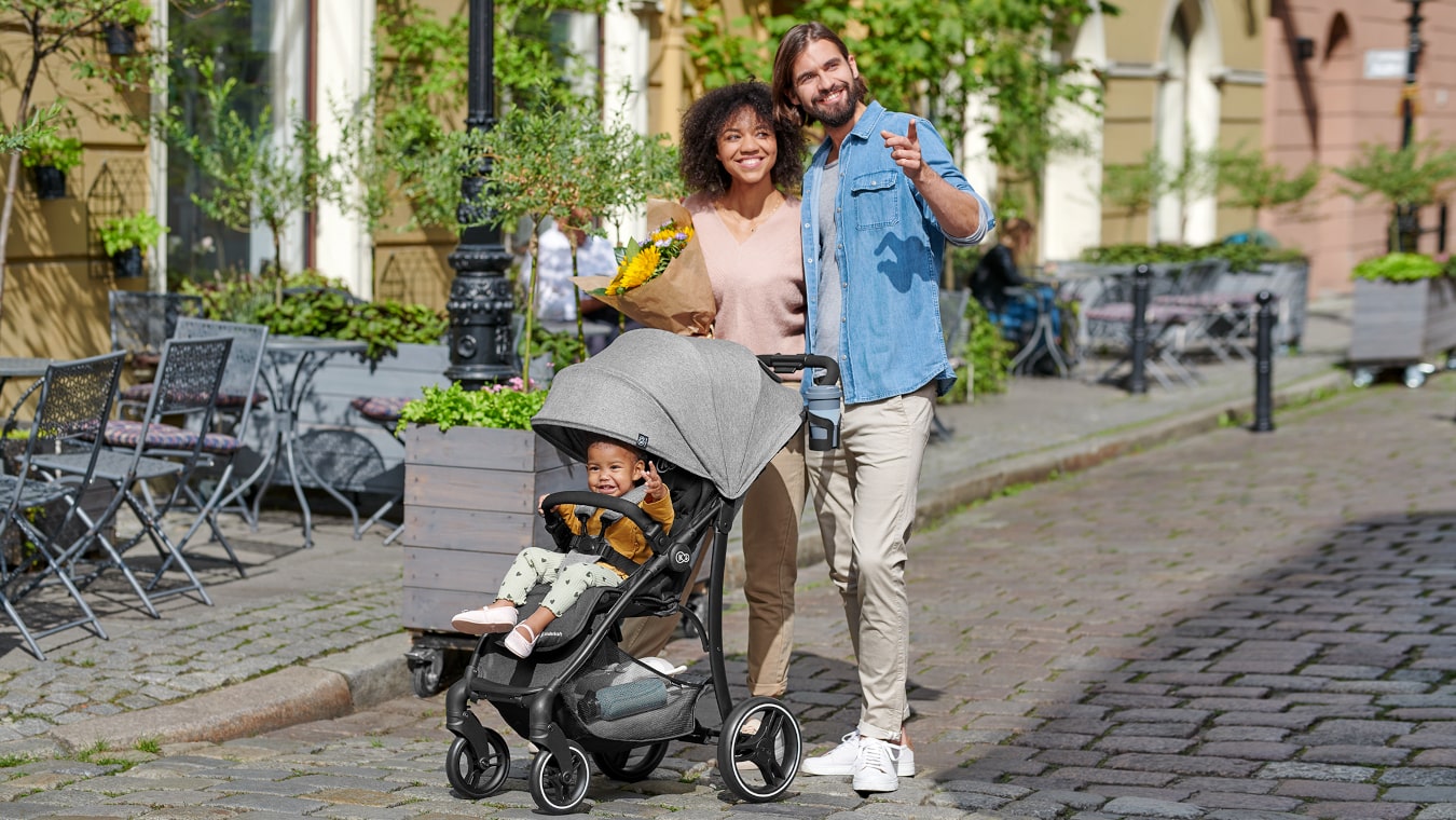 Mama z tatą i małą dziewczynką w szarym wózku spacerowym trig, są na spacerze w mieście.